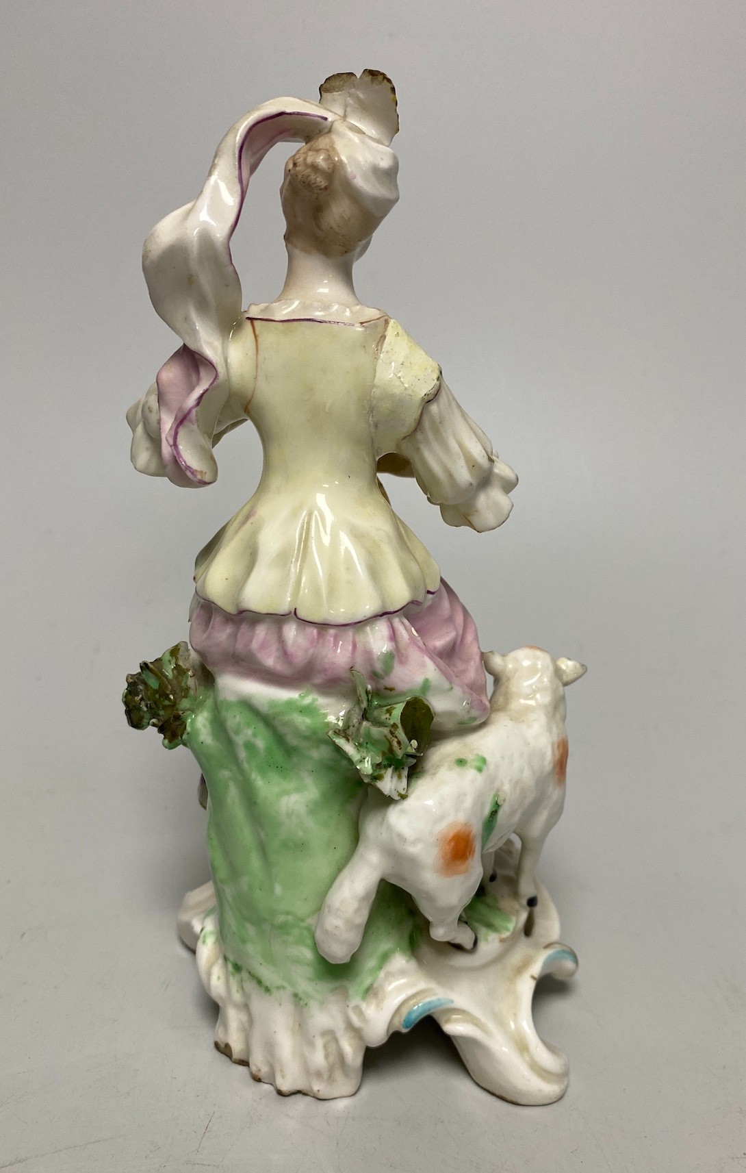 A Derby porcelain figure, modelled as a shepherdess playing a mandolin, seated on a stump, 18th century, 18cm high